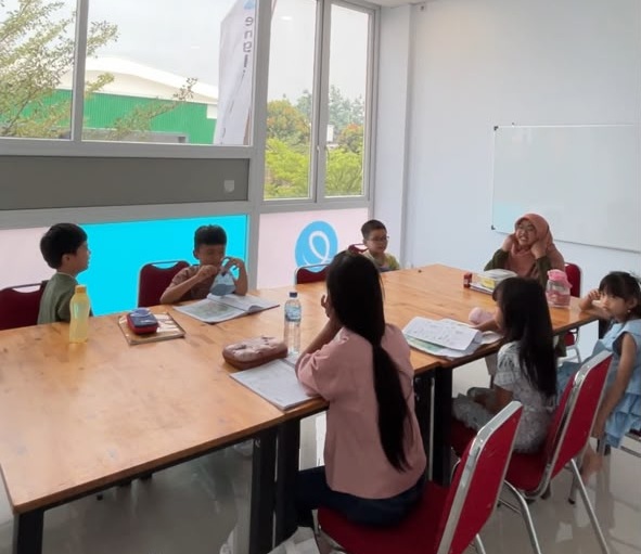 Anak-anak belajar bersama guru mengelilingi meja di ruang kelas English Central